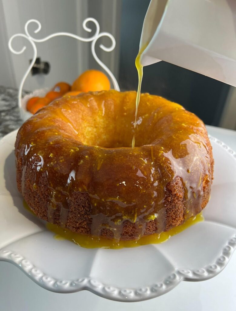 Freshly baked orange cake with orange glaze being poured over the top for a glossy finish.