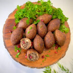 Golden brown fried kibbeh with a crispy shell, arranged on a plate, garnished with fresh parsley and served with a side of yogurt sauce