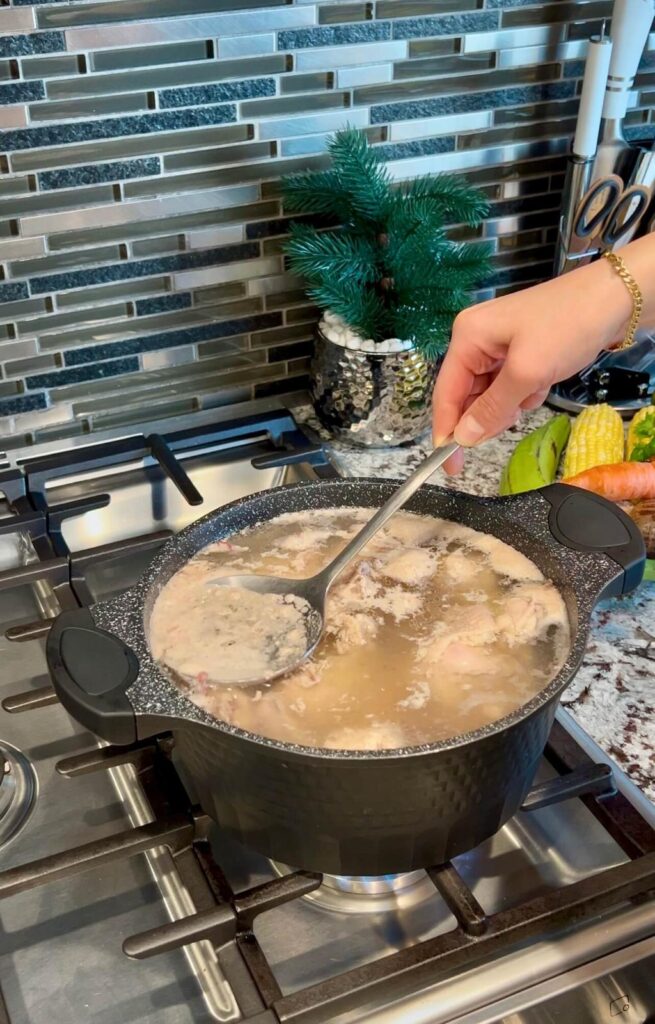 Chicken pieces boiling in a pot with onions, garlic, and cilantro, creating a flavorful broth.