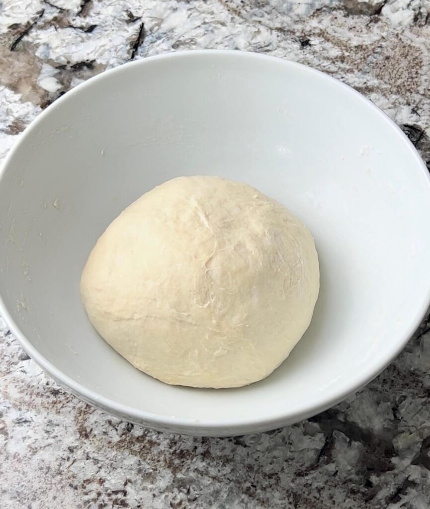 A smooth, elastic ball of dough made from flour, salt, sugar, oil, and warm water, ready to be rolled out for making cheese sambousek.