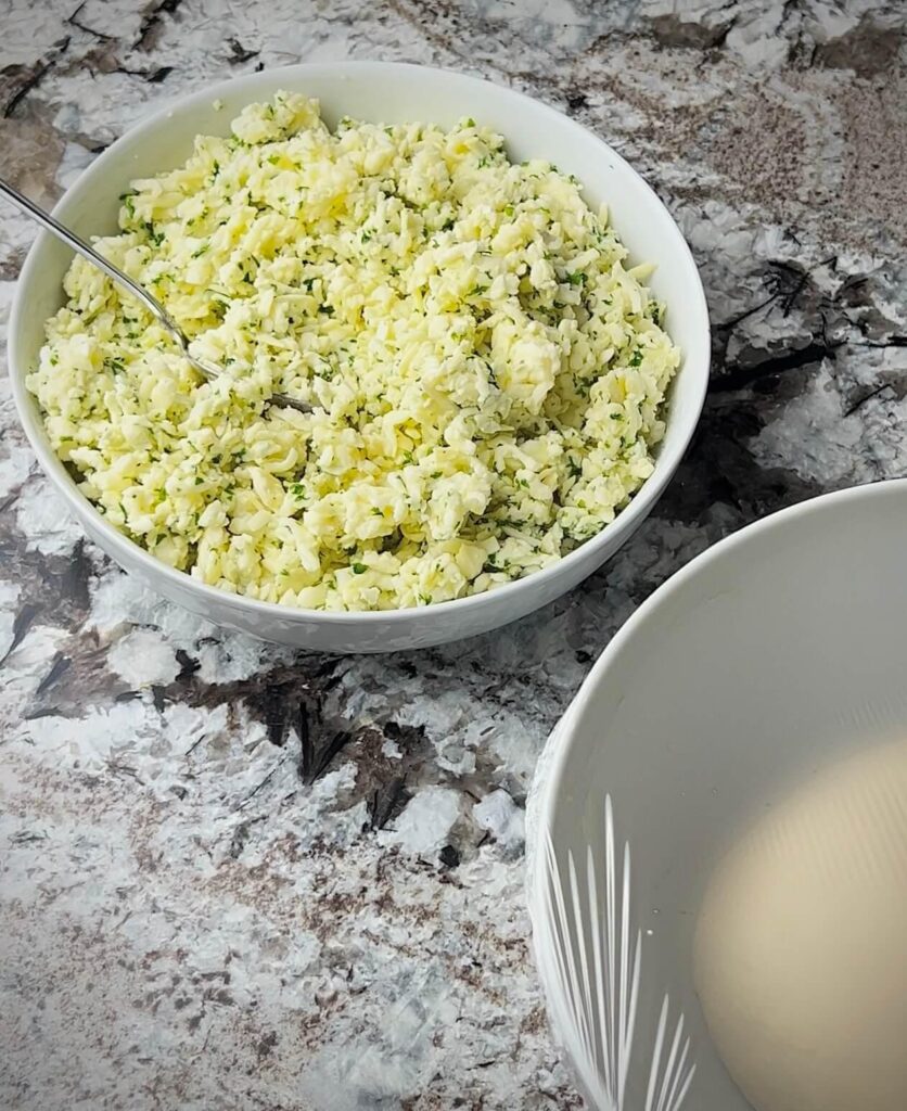 A bowl of shredded mozzarella and akkawi cheese mixed with chopped parsley, ready to be used as a savory filling for cheese sambousek.