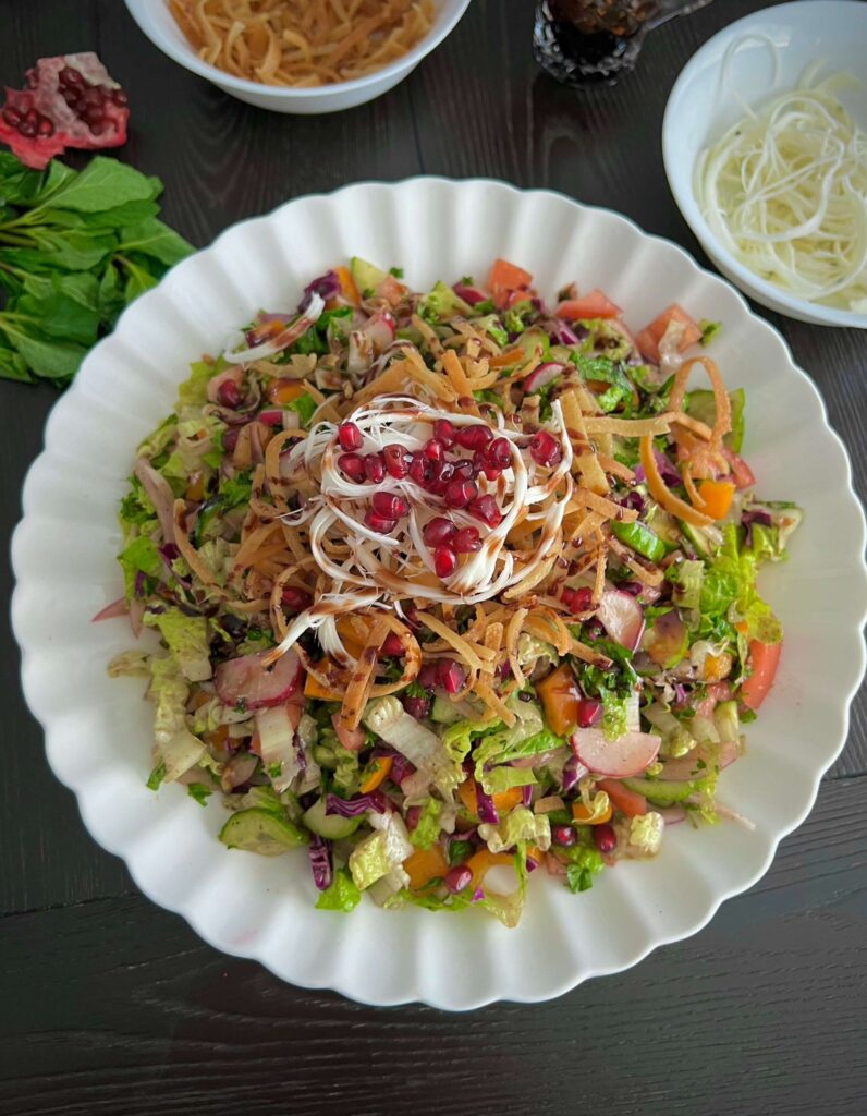 A fresh Fattoush salad with vibrant chopped vegetables, crispy fried pita bread, and a tangy dressing, garnished with pomegranate seeds and herbs.