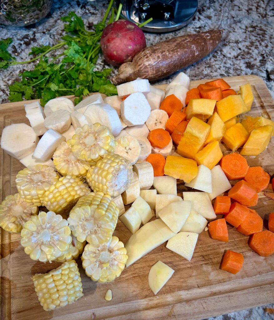 A hearty serving of Colombian Chicken Sancocho featuring yuca, potatoes, and corn, garnished with fresh cilantro and accompanied by rice and avocado.