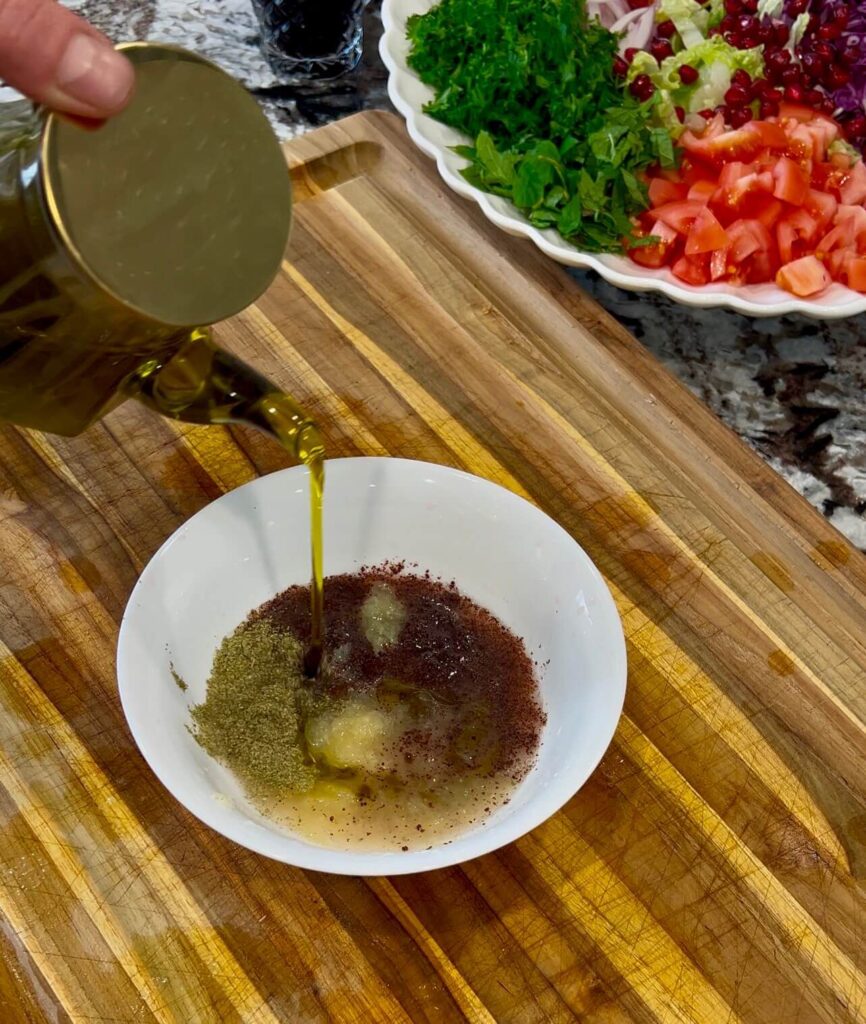 A bowl of tangy dressing made with lemon juice, olive oil, pomegranate molasses, garlic, sumac, dried mint, and spices, ready to be poured over a salad.