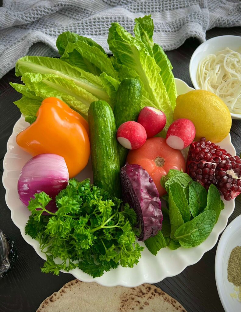 A variety of fresh vegetables including romaine lettuce, cucumbers, tomatoes, radishes, sweet peppers, red onion, and shredded red cabbage, ready to be mixed into a salad.