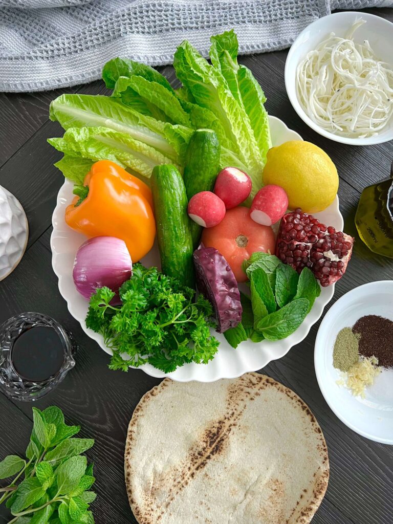 A variety of fresh vegetables including romaine lettuce, cucumbers, tomatoes, radishes, sweet peppers, red onion, and shredded red cabbage, ready to be mixed into a salad.