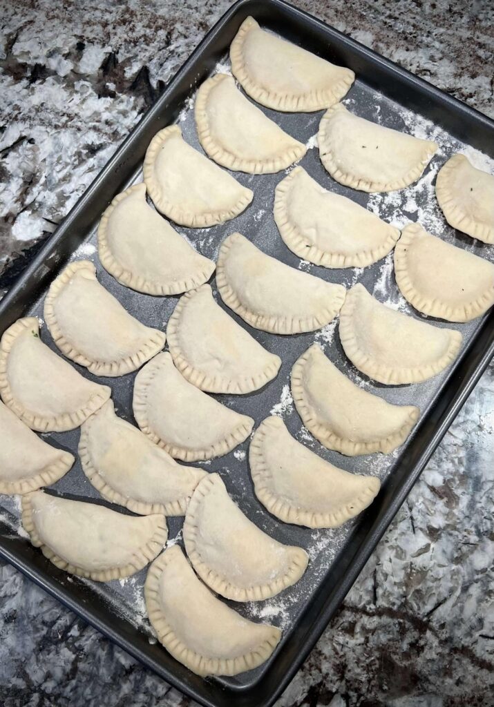 
A tray of uncooked cheese sambousek arranged in a single layer, ready to be frozen for later use.