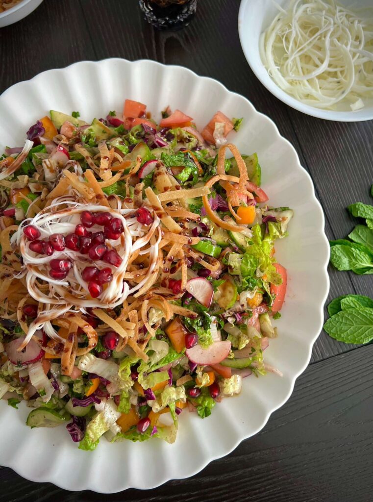 A fresh Fattoush salad with vibrant chopped vegetables, crispy fried pita bread, and a tangy dressing, garnished with pomegranate seeds and herbs.