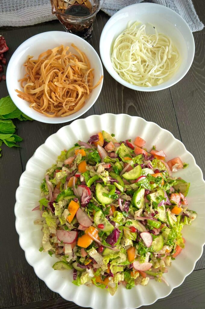 Chopped vegetables including romaine lettuce, cucumbers, tomatoes, radishes, sweet peppers, red onion, and fresh herbs like parsley and mint, prepared for a salad.