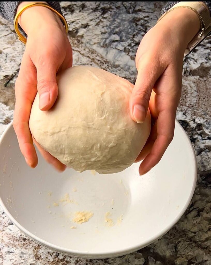 A smooth, elastic ball of dough made from flour, salt, sugar, oil, and warm water, ready to be rolled out for making cheese sambousek.