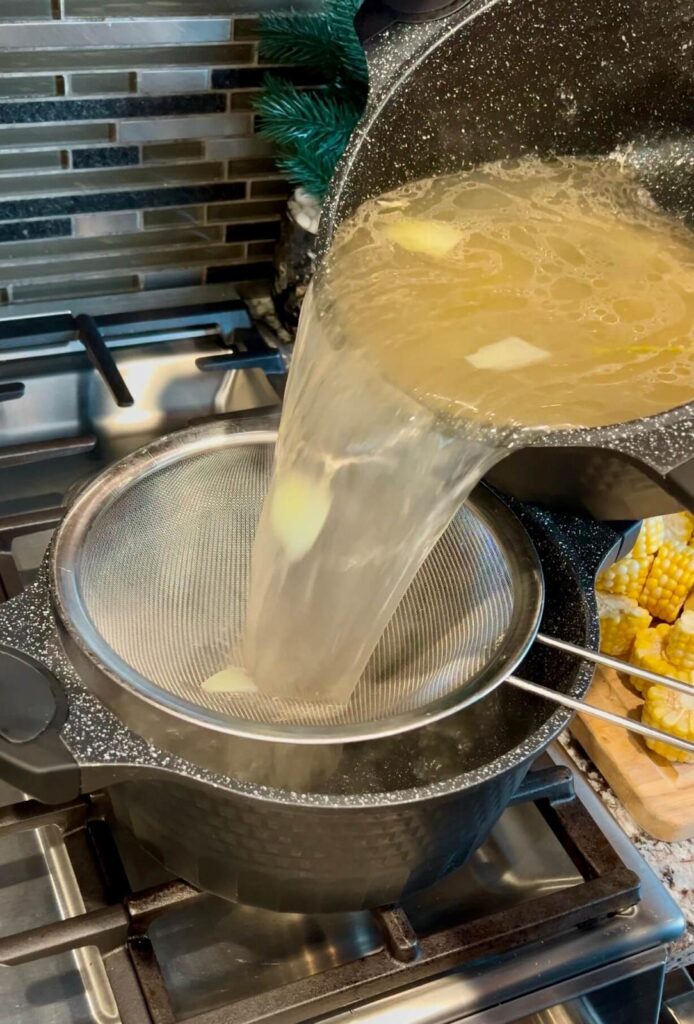 A strainer removing solids from the boiled chicken broth, leaving a clear, flavorful liquid.