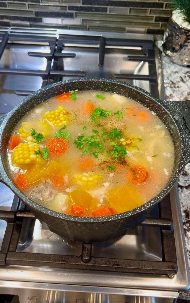 Fresh vegetables like yuca, plantains, and potatoes simmering in a pot, absorbing the rich chicken broth.

