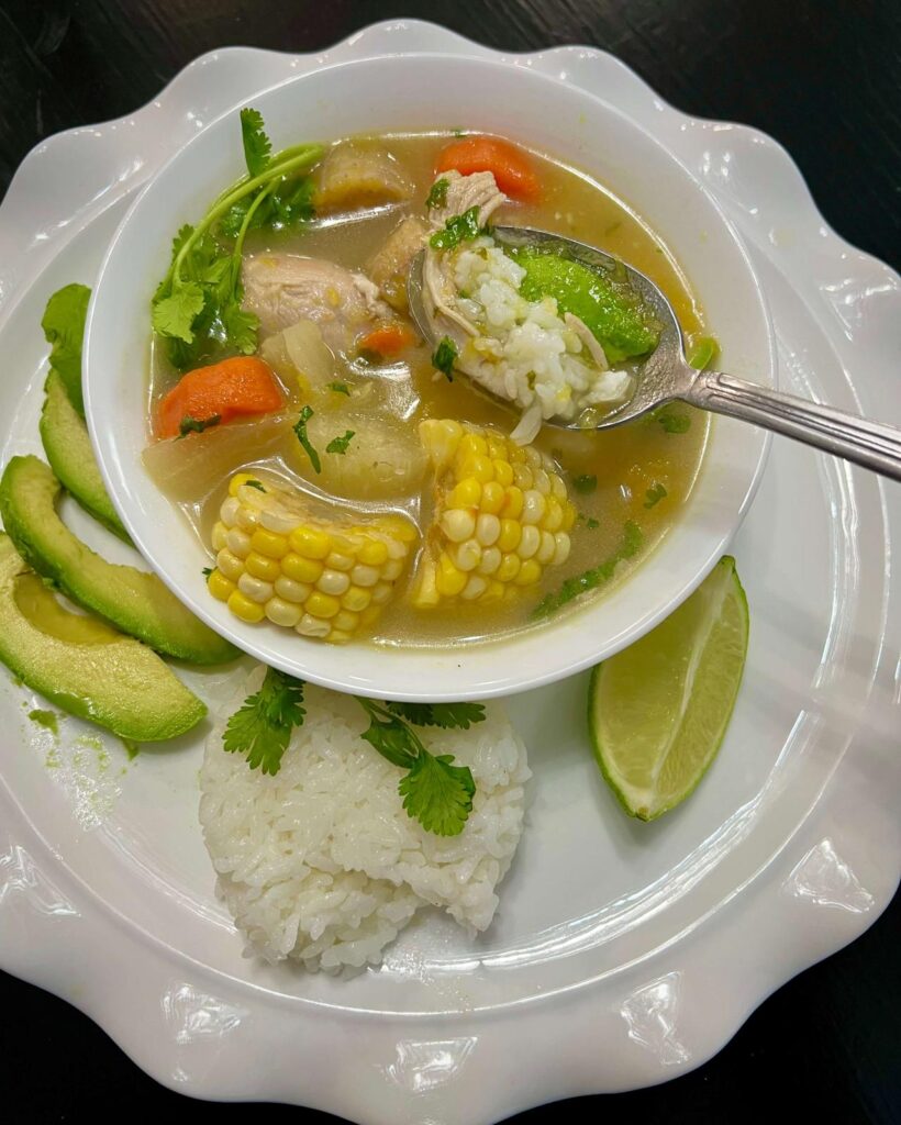 A hearty serving of Colombian Chicken Sancocho with juicy chicken, yuca, plantains, and potatoes in a rich, flavorful broth, served with rice and avocado.