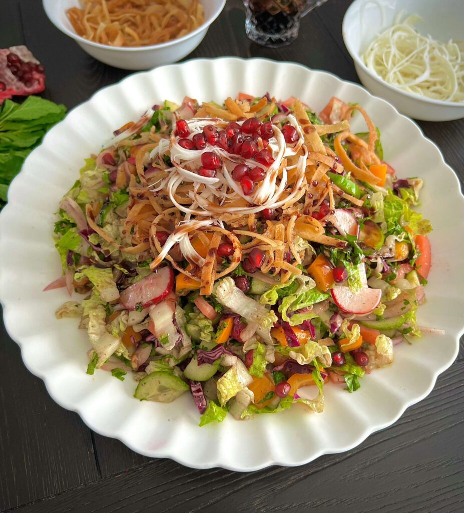 A fresh Fattoush salad with vibrant chopped vegetables, crispy fried pita bread, and a tangy dressing, garnished with pomegranate seeds and herbs.