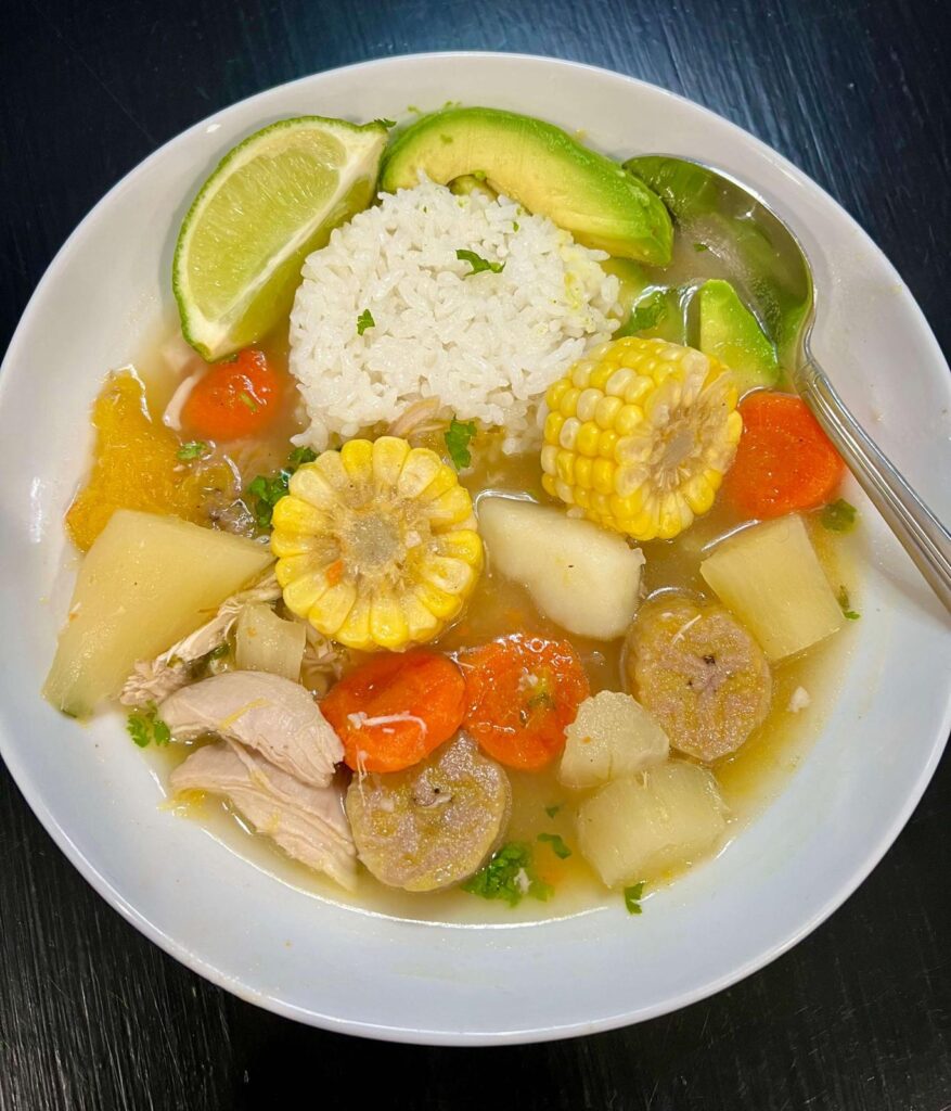 A bowl of Colombian Chicken Sancocho with tender chicken, yuca, plantains, potatoes, and corn in a golden broth, garnished with fresh cilantro.