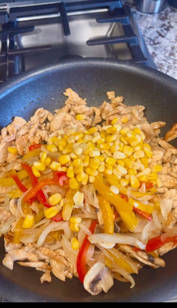 Cooking the veggies and the chicken then adding corn and mixing all together 